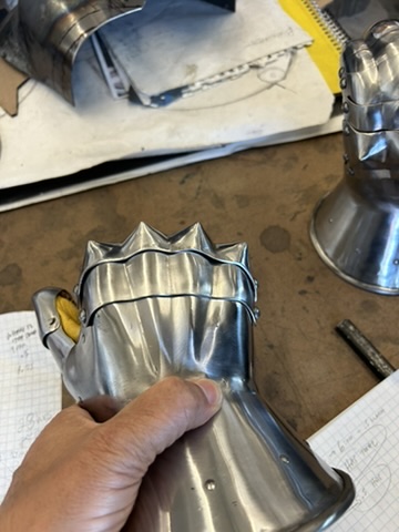 Ridged steel armor component held by hand in the workshop