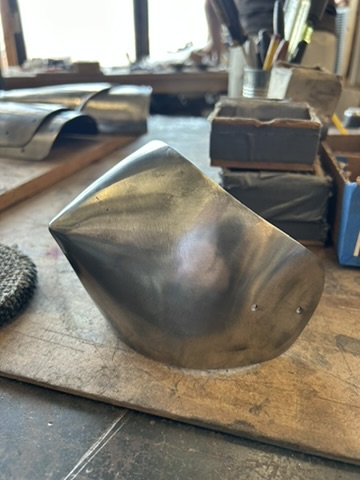 Hand-forged steel armor plate resting on a workshop bench