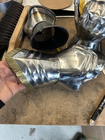 Articulated steel arm armor with etched trim held over a workshop bench