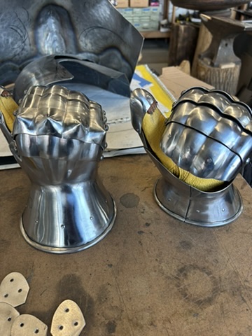 Two polished medieval helmets displayed on a workshop bench