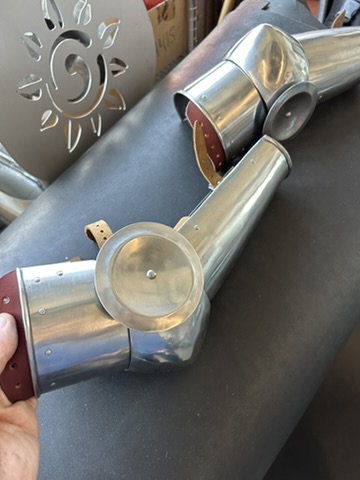 Custom steel arm pieces with leather edging shown on a dark surface